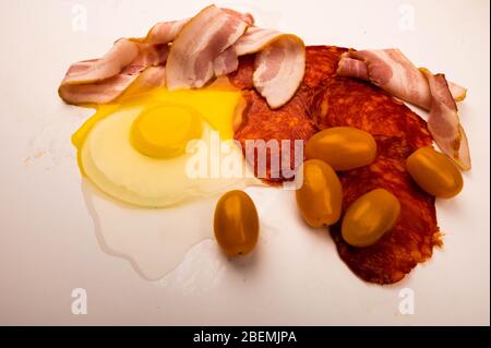 Zerbrochenes Hühnerei, Speck- und Wurstscheiben sowie Tomaten auf weißem Hintergrund. Nahaufnahme Stockfoto