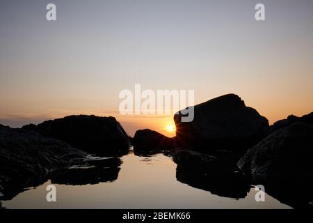 Panorama-Shot Silhouette der Meer Stack Felsformationen bei einem goldenen Sonnenuntergang mit natürlichen Sonnenstrahlen und Reflexionen Stockfoto