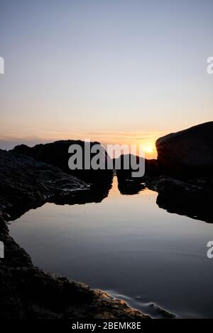 Panorama-Shot Silhouette der Meer Stack Felsformationen bei einem goldenen Sonnenuntergang mit natürlichen Sonnenstrahlen und Reflexionen Stockfoto