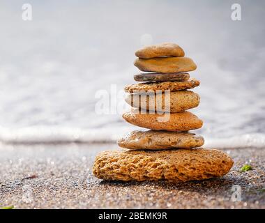 Steinpyramide auf Sand symbolisiert Zen, Harmonie, Gleichgewicht. Positive Energie. Ozean im Hintergrund Stockfoto
