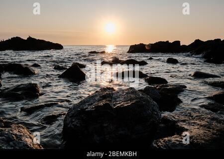 Panorama-Shot Silhouette der Meer Stack Felsformationen bei einem goldenen Sonnenuntergang mit natürlichen Sonnenstrahlen und Reflexionen Stockfoto