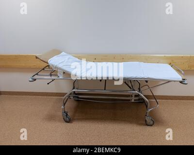 Ein Gurney-Bett, das mit einem weißen Laken bedeckt ist, oder eine Bahre auf Rollen, um bettlägerige Patienten im Krankenhausflur zu transportieren Stockfoto