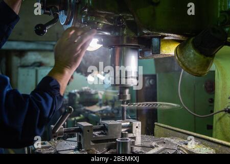 Industrieller Stahlbohrprozess mit Rauchnahaufnahme mit selektivem Fokus. Manuelle Zuführung von Hand. Werkstück im Schraubstock auf Tisch. Hoher Kontrast mit Hintergrundfarbe Stockfoto