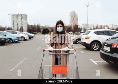 Junge Frau trägt Schutzmaske gegen Coronavirus 2019-nCoV und schiebt einen Einkaufswagen. Stockfoto