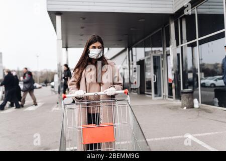 Junge Frau trägt Schutzmaske gegen Coronavirus 2019-nCoV und schiebt einen Einkaufswagen. Stockfoto