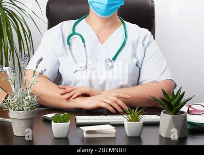 Arzthandschuhe sitzen an einem weißen Arbeitstisch in seinem Büro, Konzept der Patientenaufnahme in der Klinik, Hände vor der Brust verbunden, fokussierte Pose Stockfoto