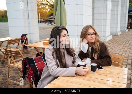 Zwei attraktive Freundinnen sitzen im Café draußen und trinken Kaffee Stockfoto