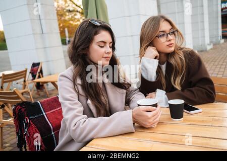 Zwei attraktive Freundinnen sitzen im Café draußen und trinken Kaffee Stockfoto