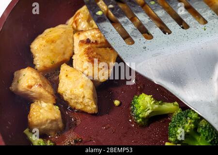 In einer Pfanne werden vegetarisch simuliertes Huhn und frischer Brokkoli gekocht. Eine Nahaufnahme zeigt die Details in der Nahrung, blubbernde Öle auf dem Stockfoto
