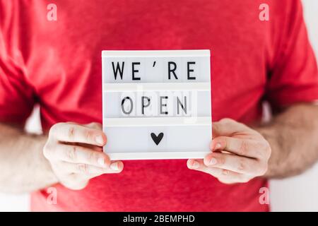 Ende der Quarantäne. Mann mit Leuchtkasten mit Grußtext Wir sind offen in seinen Händen. Hotel, Café, lokaler Shop, Service-Besitzer begrüßen Gäste af Stockfoto