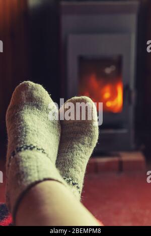 Füße Beine im Winter Kleidung Wolle Socken am Kamin Hintergrund. Frau sitzt zu Hause auf Winter oder Herbst am Abend entspannen und aufwärmen. Winter und Kälte Konzept. Hygge Heiligabend Stockfoto