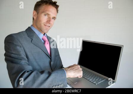 Geschäftsmann, der auf die Kamera stehend mit Laptop-Computer mit leerem Bildschirm Stockfoto