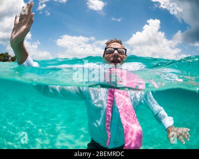 Über-unter Ansicht des Geschäftsmannes, der seine Hand oben hält, um Hilfe zu rufen versucht, in klarem türkisfarbenem Wasser über Wasser zu halten Stockfoto