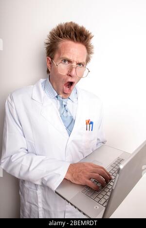 Verrückter Wissenschaftler mit verrücktem Ausdruck, um seine Haare auf die Kamera mit seinem Laptop-Computer passen Stockfoto