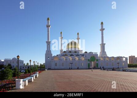 NUR-SULTAN, ASTANA, KASACHSTAN - 3. JUNI 2015: Weiße nur Astana Moschee mit goldener Kuppel. Leeres Quadrat mit Bänken und Blumenbeet von rot und lila Stockfoto