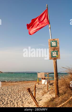 Strand von SES Illetes, Formentera, Balearen, Spanien. Rote Flagge am Strand von Ses Illetes, die auf Gefahr hinweist. Im Hintergrund das schöne Meer Stockfoto