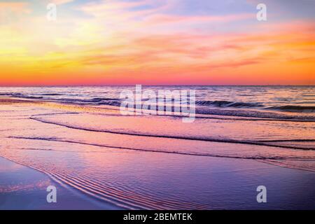 Beobachten Sie die schönen Farben des Sonnenuntergangs, die sich von den Wellen am Strand spiegeln Stockfoto