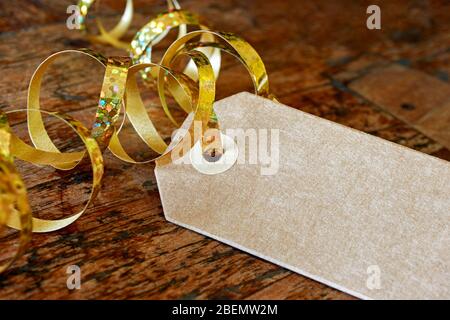 Leerer brauner Geschenkanhänger mit lockig goldenem Band. Kraftpapier Karton Etikett auf Holz mit Kopierfläche. Shopping, Verkauf, Feier oder weihnachtskonzept. Stockfoto