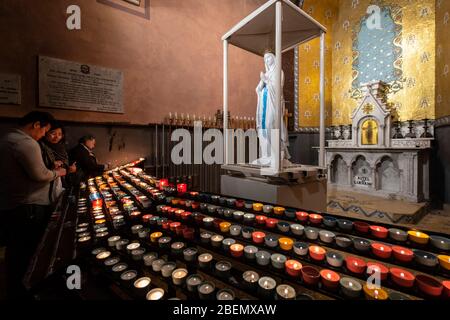 Menschen, die zur Statue der Jungfrau Maria beten, nachdem sie in der Basilika unserer Lieben Frau vom Rosenkranz im Heiligtum unserer Lieben Frau von Lourdes, Frankreich, eine Kerze angezündet haben Stockfoto