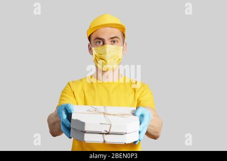 Paket an die Tür. Kurier in gelber Uniform, Schutzmaske und Handschuhe liefert Pizza und Kaffee zum Mitnehmen. Lieferservice unter Quarantäne. Kopieren Stockfoto
