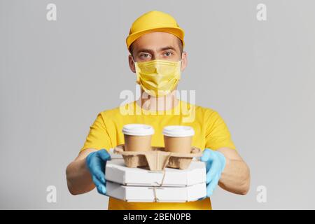 Paket an die Tür. Kurier in gelber Uniform, Schutzmaske und Handschuhe liefert Pizza und Kaffee zum Mitnehmen. Lieferservice unter Quarantäne. Kopieren Stockfoto