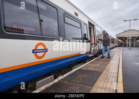 Passagier, der mit einem Fahrrad/Fahrrad am Bahnhof Clapham Junction mit dem Overground-Logo in einen TFL London Overground-Zug der Klasse 378 einsteigen wird Stockfoto