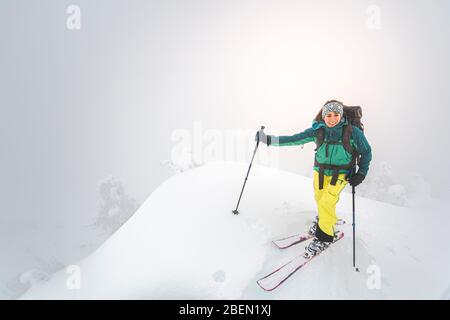 Junge Frau lächelt im Backcountry auf dem schneebedeckten Gipfel in Squamish Stockfoto