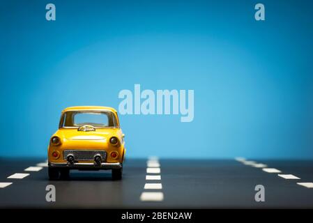 Vorderansicht eines gelben Spielzeugautos auf blauem Hintergrund und auf einer Asphaltstraße. Stockfoto