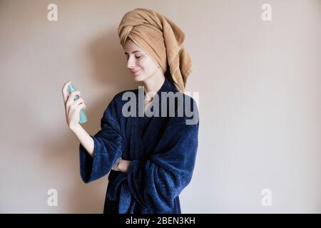 Frau in einem Gewand und mit einem Handtuch auf dem Kopf trägt Kosmetik auf die Haut Stockfoto