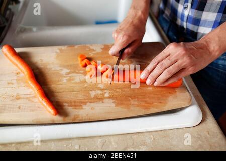 Nahaufnahme der Hände einer Frau, die eine Karotte auf einem Hackblock schneidet Stockfoto