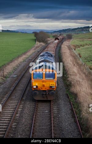 GB Eisenbahnlokomotive der Baureihe 66 66704 mit einem Güterzug, der Material für Network Rail trägt, vorbei an New Cumnock, Südwestschottland. Stockfoto