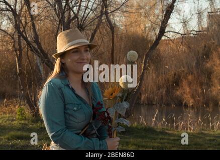 Junge blonde Haarfrau mit Blumenstrauß und Cowboy-Kleid auf dem Feld Stockfoto