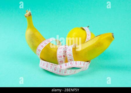 Verschiedene Arten von Obst, wie Äpfel und Bananen liegen auf einem Fuß und sind in einem Maßband verpackt - Konzept für eine gesunde Gewichtsabnahme Stockfoto