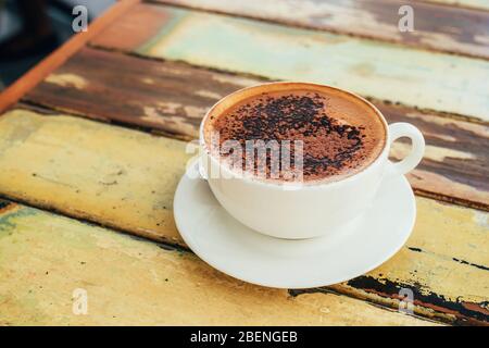 Weiße Tasse Cappuccino mit Schokoladenpulver auf dem rustikalen Holztisch. Stockfoto