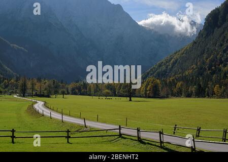 Schöne Landschaft mit grünem Gras, Straße und Holzzaun im Vordergrund, und mit den Berggipfeln und Wolken im Hintergrund Stockfoto