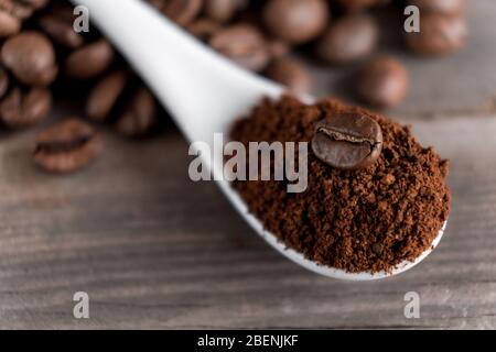 Weißer Keramiklöffel mit gemahlenem Kaffee auf Holzgrund gebratene Arabica-Körner. Stockfoto