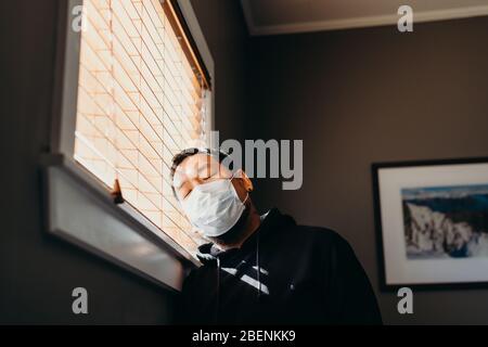 Asian Mann in Isolation Gefühl traurig und müde. Mann in medizinischer Maske gezwungen, im Haus zu bleiben, als Folge der Einschränkungen durch die Corona verursacht Stockfoto