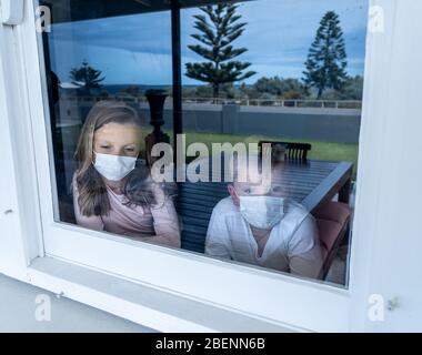 COVID-19-Sperrungen. Traurige Kinder mit Gesichtsmaske, die während der Quarantäne zu Hause durch das Fenster schauen. Kinder fühlen sich traurig, als die Schule geschlossen ist. Coronaviru Stockfoto