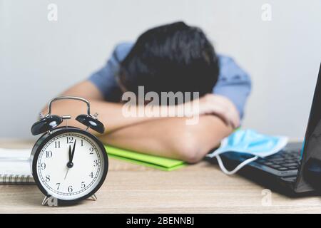 Arbeit von zu Hause aus während des Ausbruchs des Virus. Wecker auf dem Tisch um Mitternacht mit Unschärfe arbeitet der Geschäftsmann von zu Hause aus und Er schläft bec Stockfoto