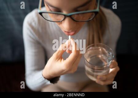 Eine junge kranke weiße Frau zu Hause schluckt ihre medizinischen Behandlung Pillen mit einem Glas Wasser. Stockfoto