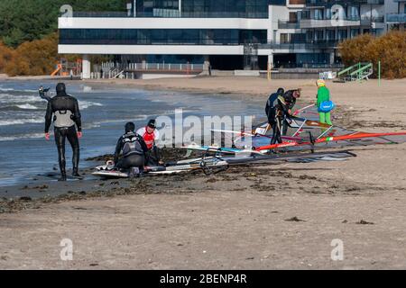 Tallinn, Estland - 18. Oktober 2008: Windsurfer in Anzügen untersuchen Boards mit einem Segel auf dem Sand am Meer. Verschwommenes Hotel im Hintergrund. Stockfoto