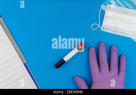 Flache Lay-Zusammensetzung mit Blutprobe und antiviraler medizinischer Maske auf blauem Hintergrund. Hand in einem medizinischen Gummihandschuh Stockfoto