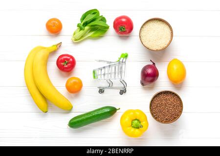 Verschiedene gesunde Lebensmittel - Buchweizen, Reis, gelbe Paprika, Tomaten, Bananen, Salat, grün, Gurke, Zwiebeln, Warenkorb auf weißen Holzbackgr Stockfoto