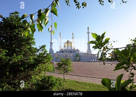 NUR-SULTAN, ASTANA, KASACHSTAN - 3. JUNI 2015: Weiße nur Astana Moschee mit goldener Kuppel aus einem besonderen Blickwinkel aus grünen Blättern und Bäumen Stockfoto