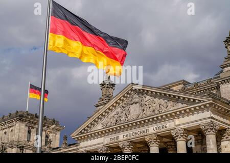 Berlin, Deutschland. April 2020. 04/09/2020, Berlin, das Berliner Reichstagsgebäude von Baumeister Paul Wallot am Platz der Republik an einem sonnigen Frühlingssafttag mit bewölktem Himmel. Detail des Gebäudes mit dem Schriftzug 'dem Deutschen Volk' und der winkenden deutschen Flagge. Der Reichstag ist Sitz des Deutschen Bundestages mit Plenarbereich. Kredit: dpa/Alamy Live News Stockfoto