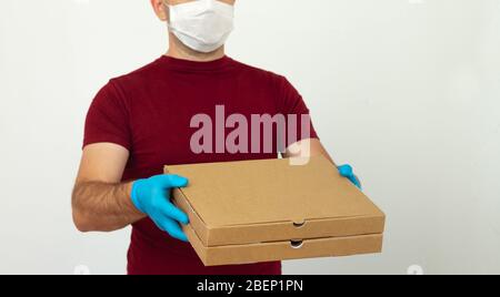 Ein Kurier in medizinischen Handschuhen und Maske hält Pizzakartons. Pizzalieferung während der Quarantäne. Kontaktlose Lieferung Stockfoto