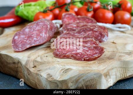 In Scheiben geschnittenes Fuet auf dem Küchenbrett, frische Tomaten Cherry Nahaufnahme. Gesundes mediterranes Food Konzept. Stockfoto