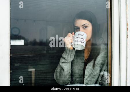 Junge Frau zu Hause zu bleiben Kaffee / Tee trinken, Blick durch das Fenster.Starting den Tag, Morgen Ritual.Quaratine Selbstisolierung concept.Worried wom Stockfoto