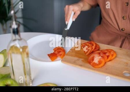 Nahaufnahme der Hand der Frau, die mit einem Küchenmesser frische Tomaten in Scheiben auf den Teller legt Stockfoto