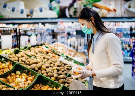 Frau mit hygienischen Maske Kauf im Supermarkt Lebensmittelgeschäft für frische Grüns, Budget-Shopping für Lieferungen während der Pandemie.Kauf von Bio vegetabl Stockfoto